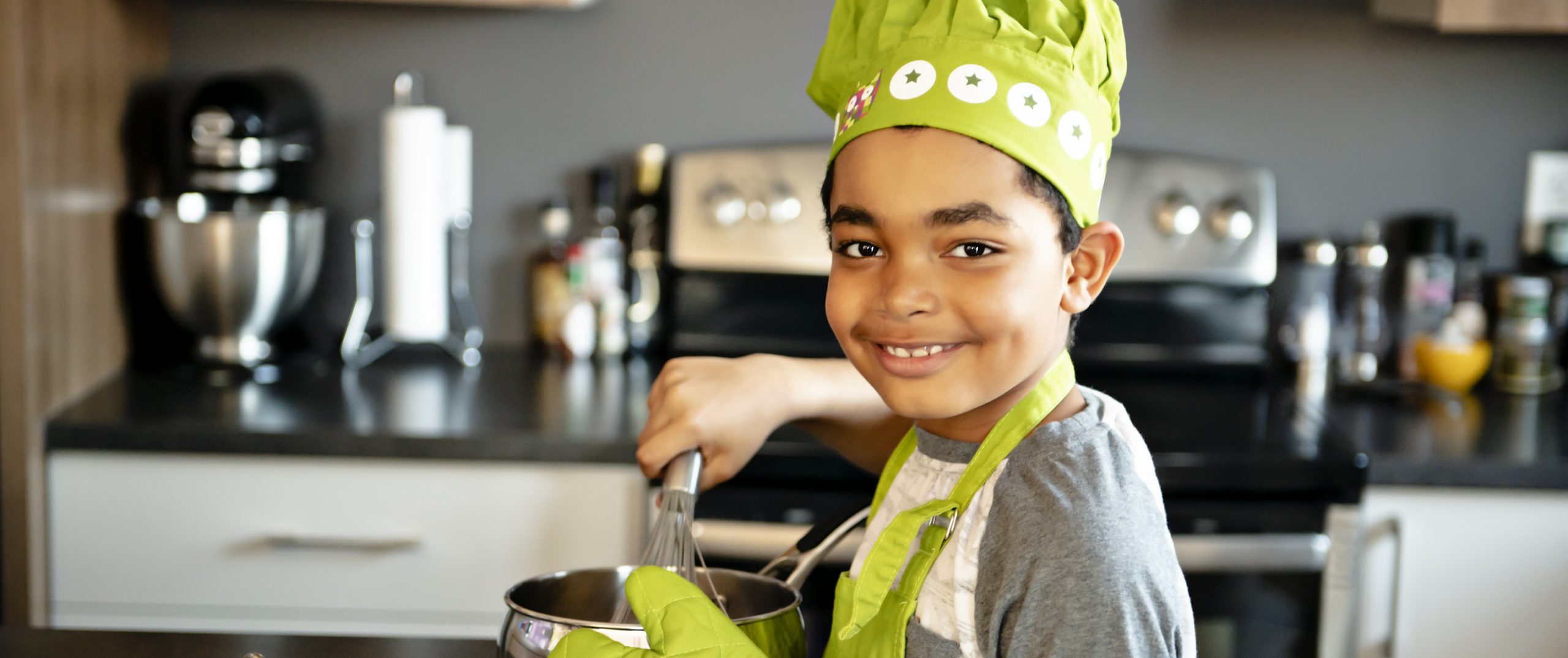 Child whisking and wearing a green chef's hat