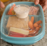 plastic container with cheese, crackers, fruit, and baby carrots