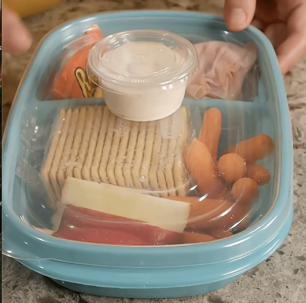 plastic container with cheese, crackers, fruit, and baby carrots