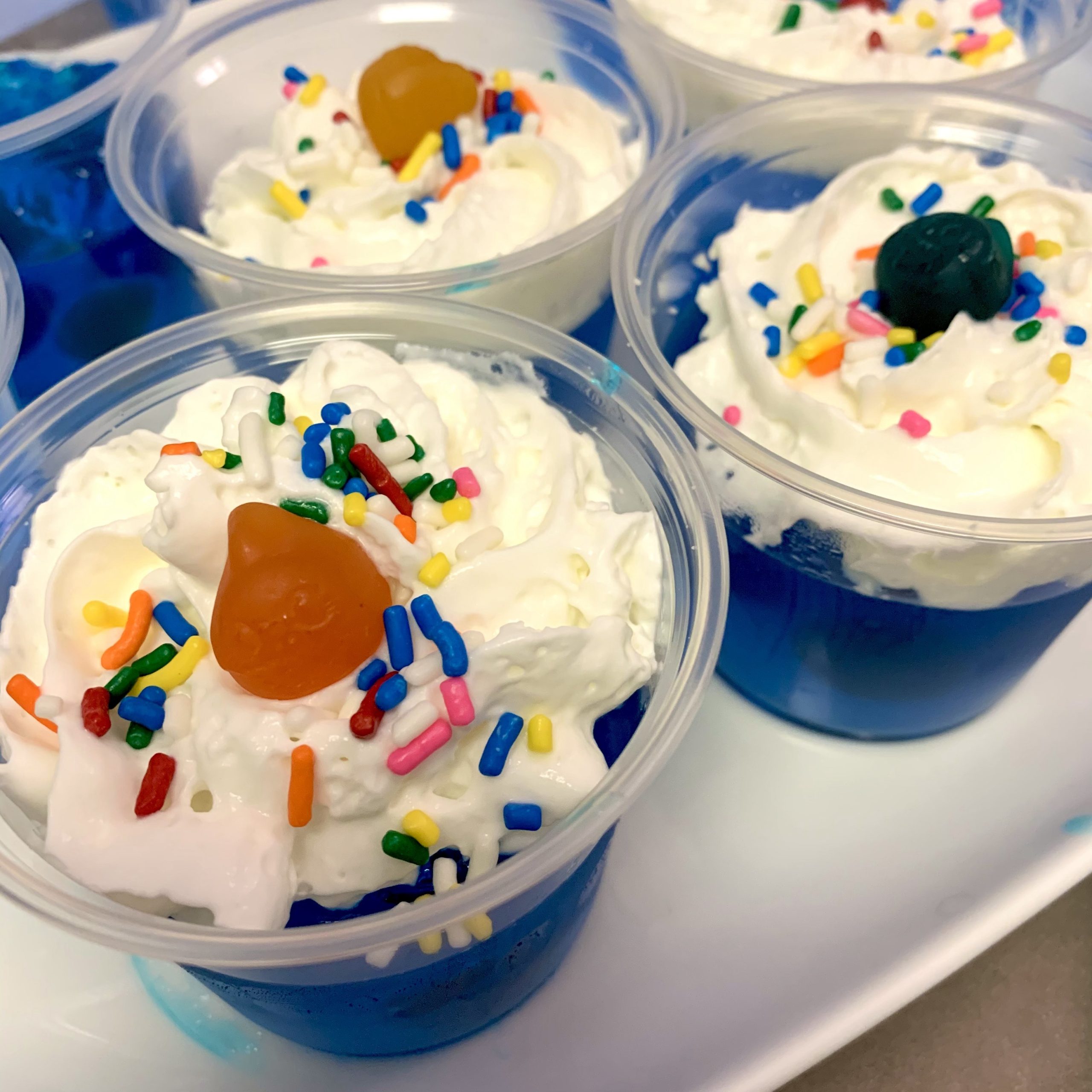 Plastic cups filled with blue Jell-O, whipped cream, sprinkles, and shark fruit snacks