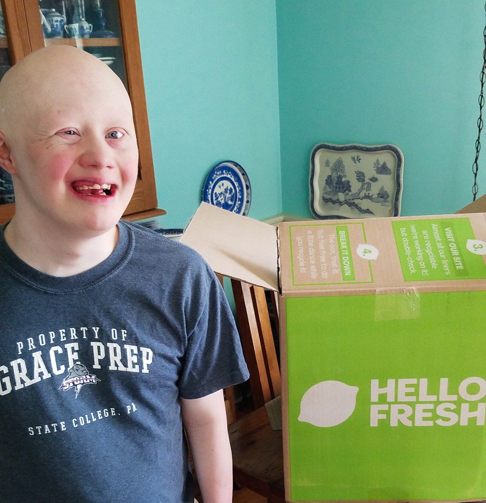 Sam, man with Down syndrome, smiling in front of a green HelloFresh box