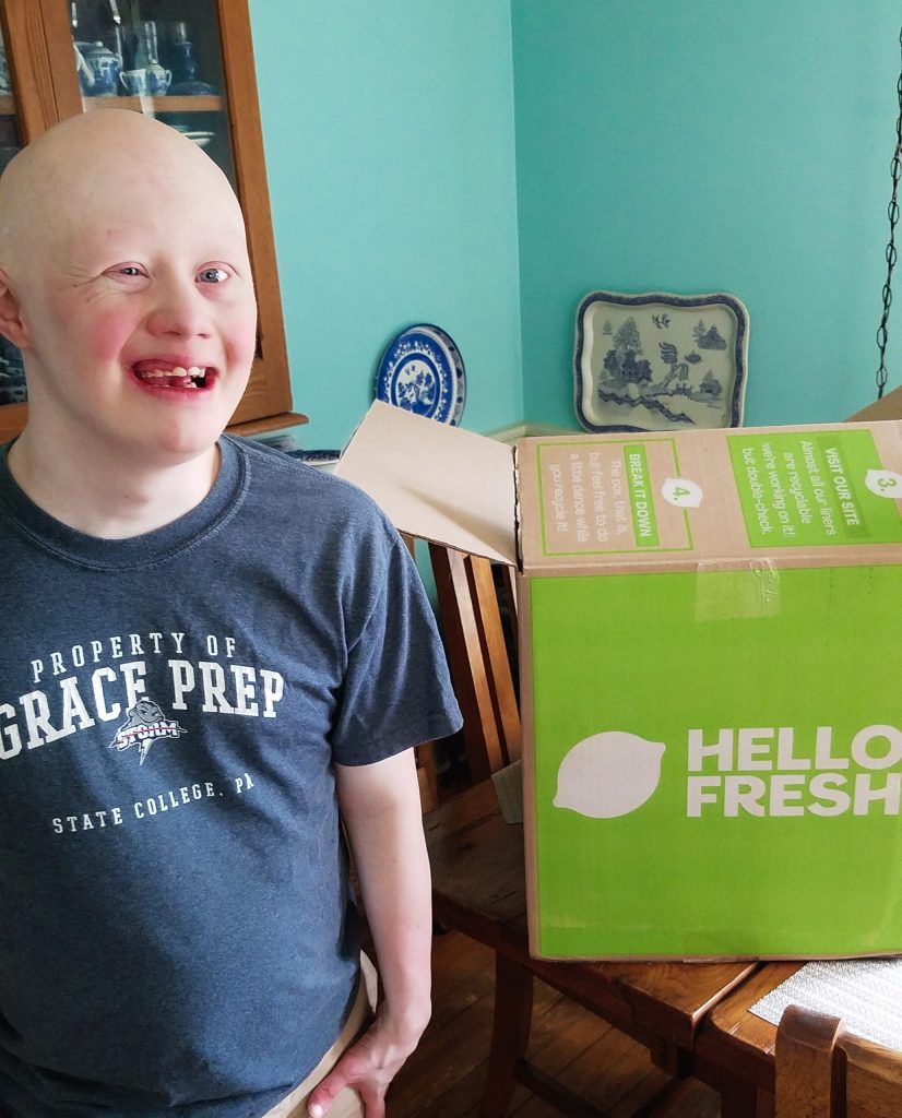 Sam, man with Down syndrome, smiling in front of a green HelloFresh box