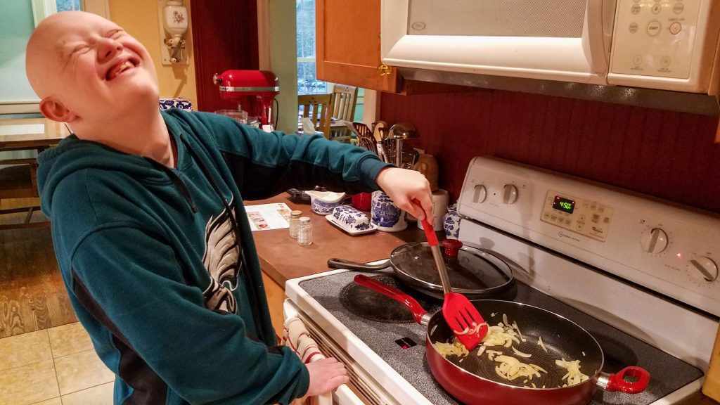 Sam, man with Down syndrome, laughing as he stirs onions in a saute pan
