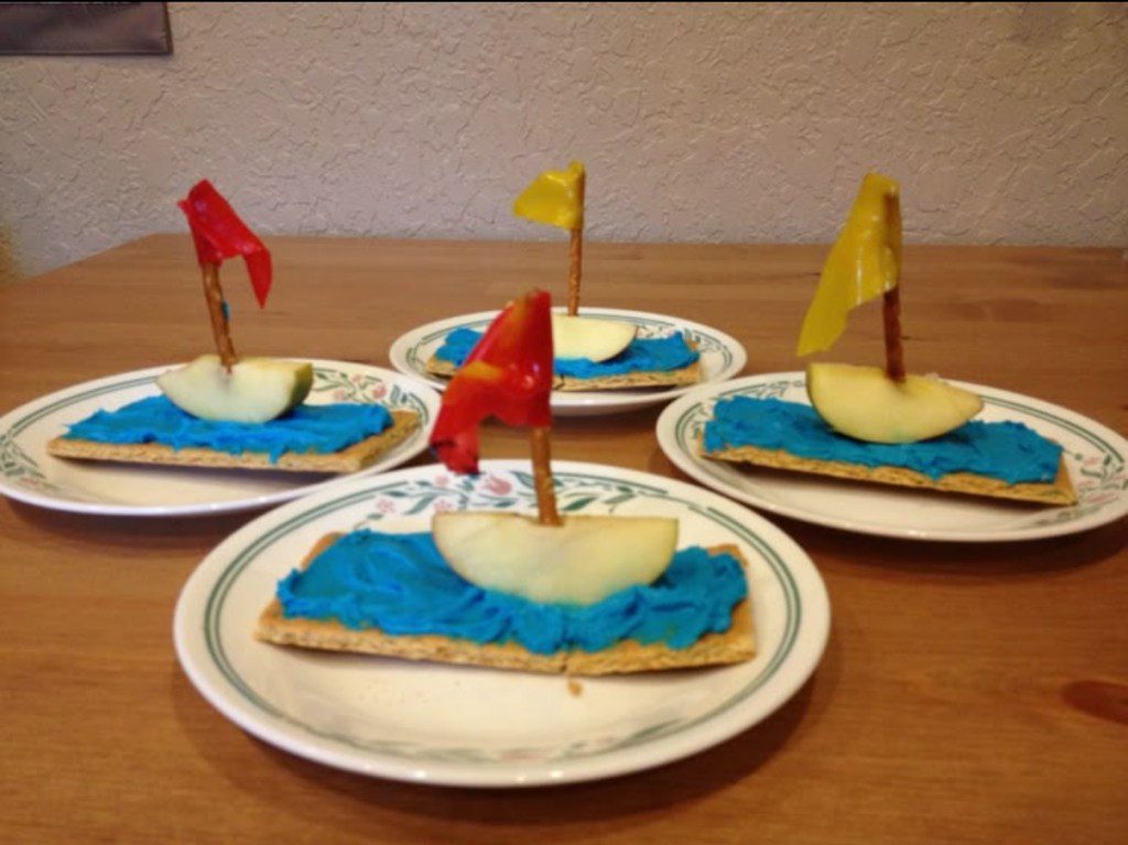 pirate ship apple snacks made with an apple slice on a graham cracker with blue frosting and a pretzel stick mast